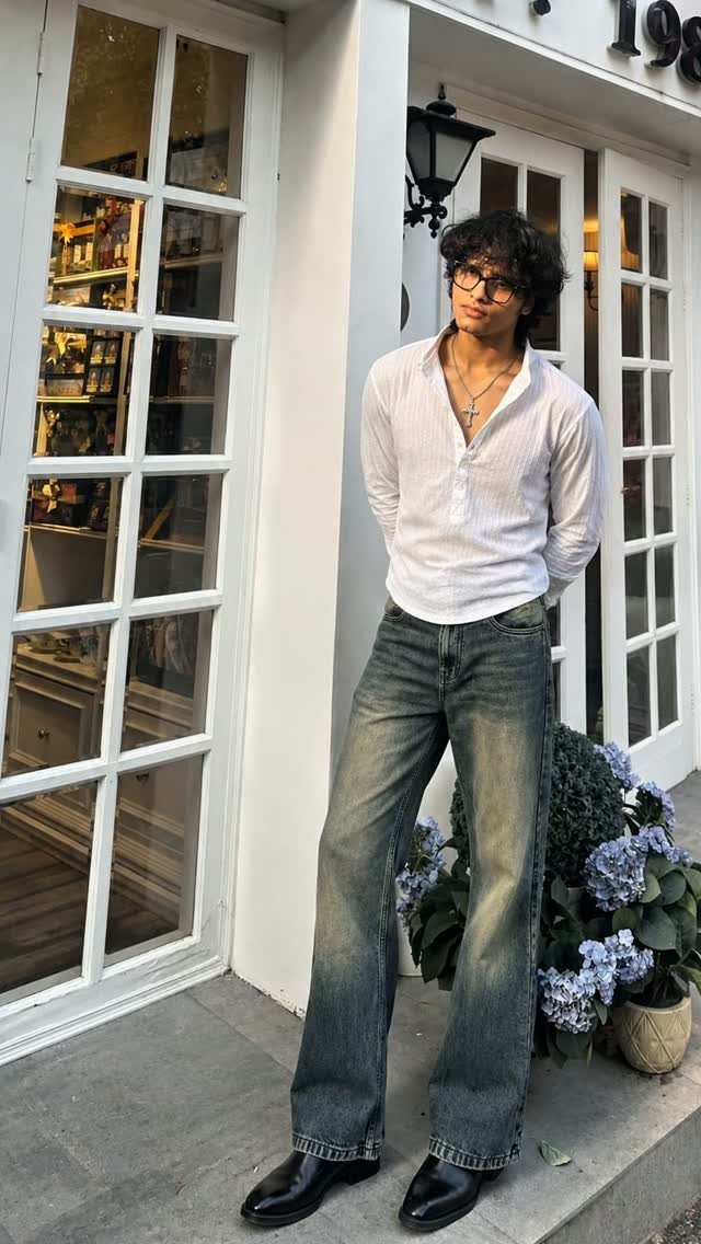 Man wearing a white shirt, blue jeans, and black leather Chelsea boots standing outside.