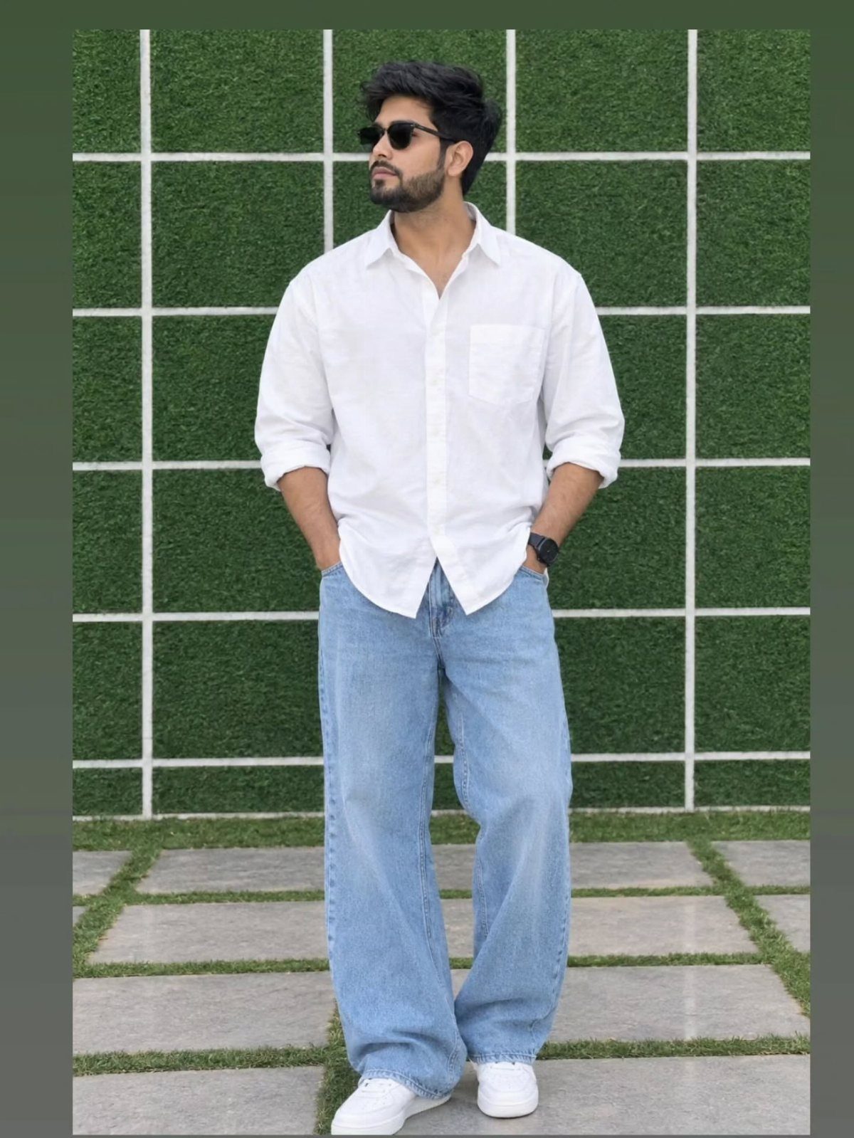Man wearing a white button-down shirt and light blue wide-leg jeans standing outdoors.
