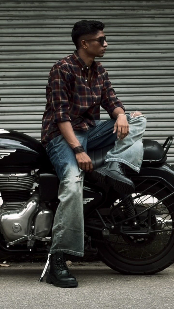 Man in a plaid shirt and blue jeans sitting on a black motorcycle.