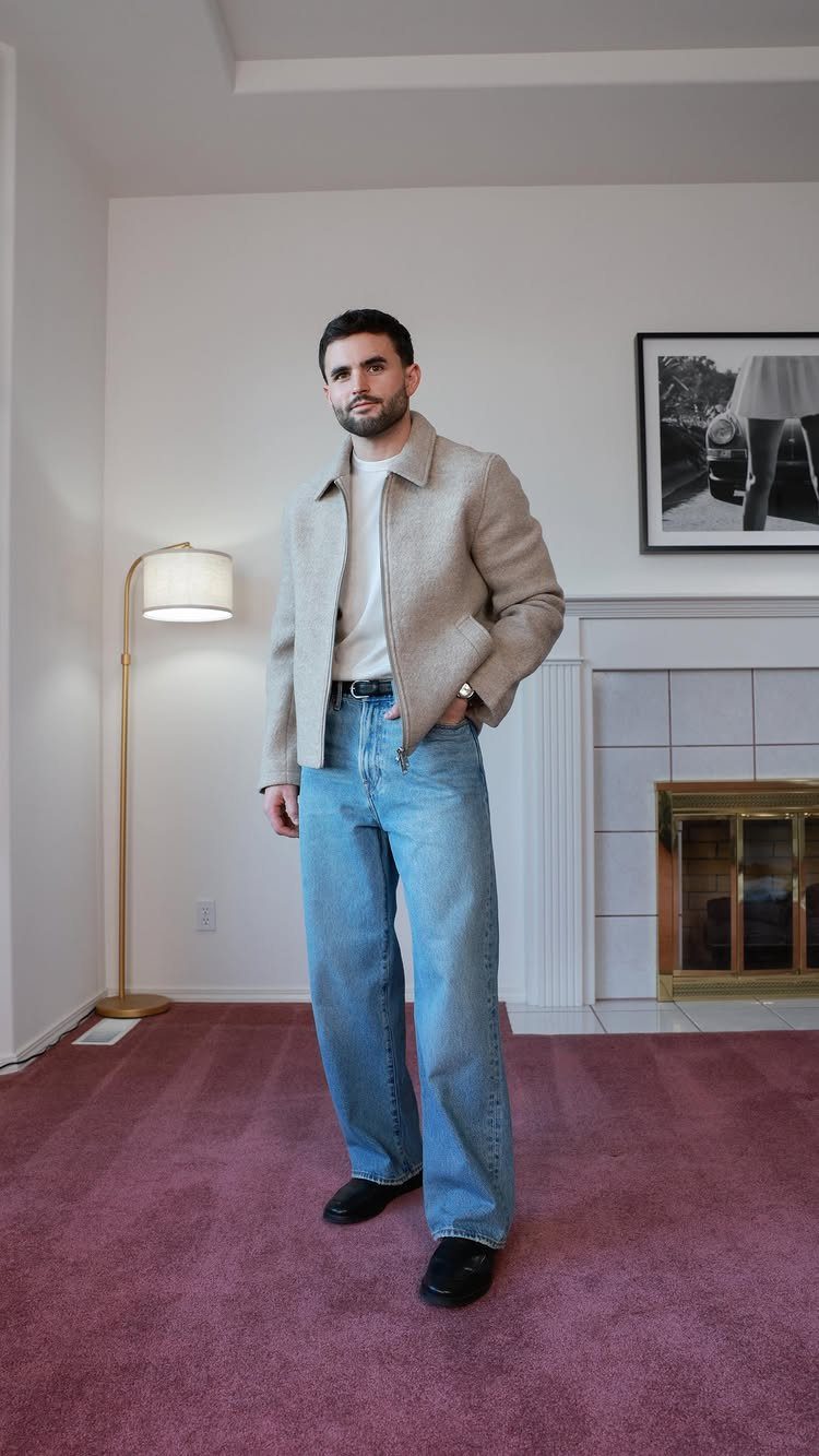 A man posing in light blue wide-leg jeans, a beige jacket, and black shoes.