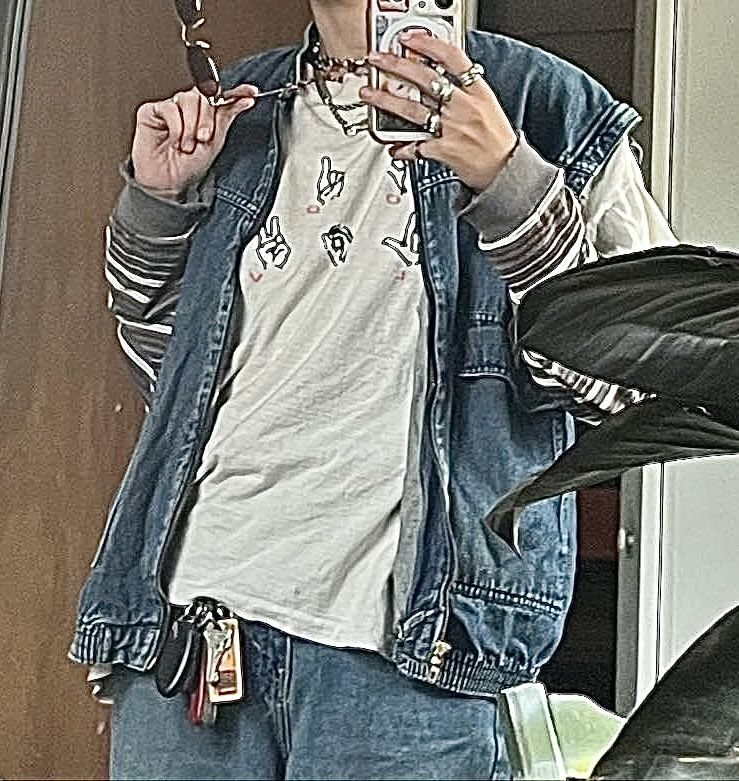 Person wearing a blue denim vest over a white graphic t-shirt and blue jeans.