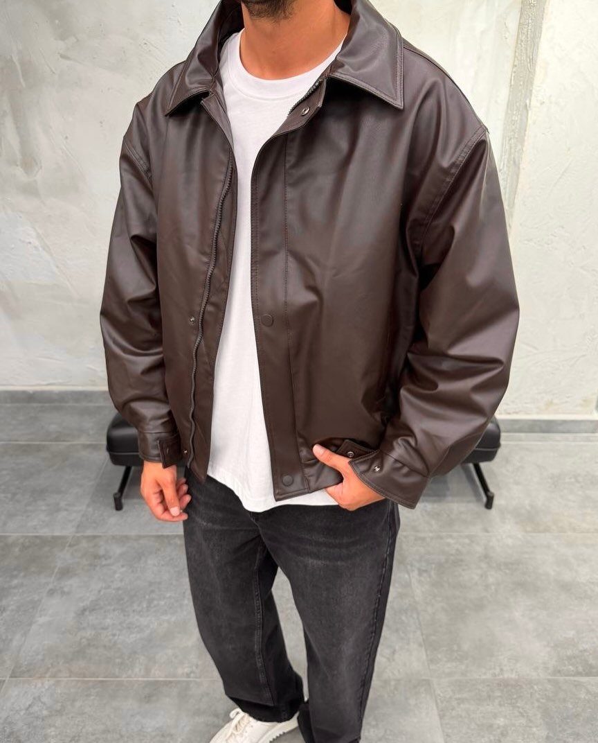 A person wearing a brown leather jacket, white t-shirt, and black jeans.
