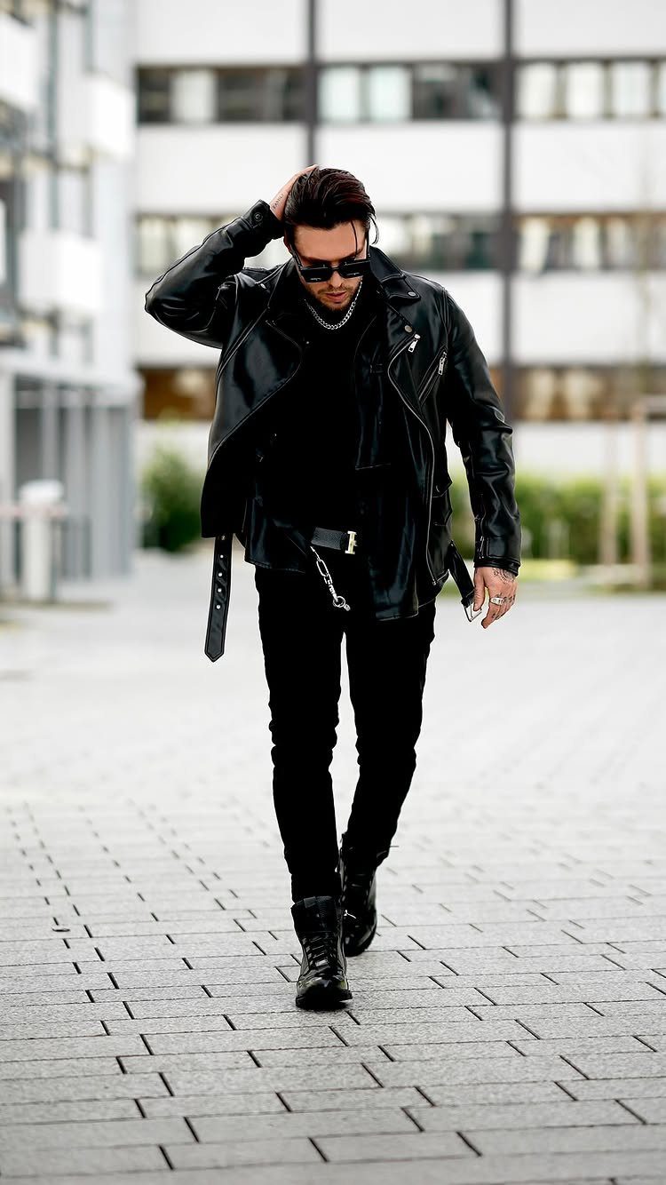 Man in black leather jacket, black trousers, and combat boots walking outdoors.