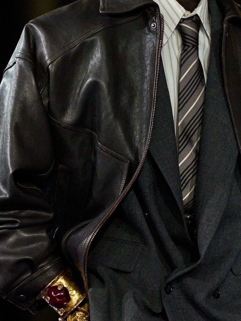 A person wearing a dark leather jacket over a grey suit and striped tie.