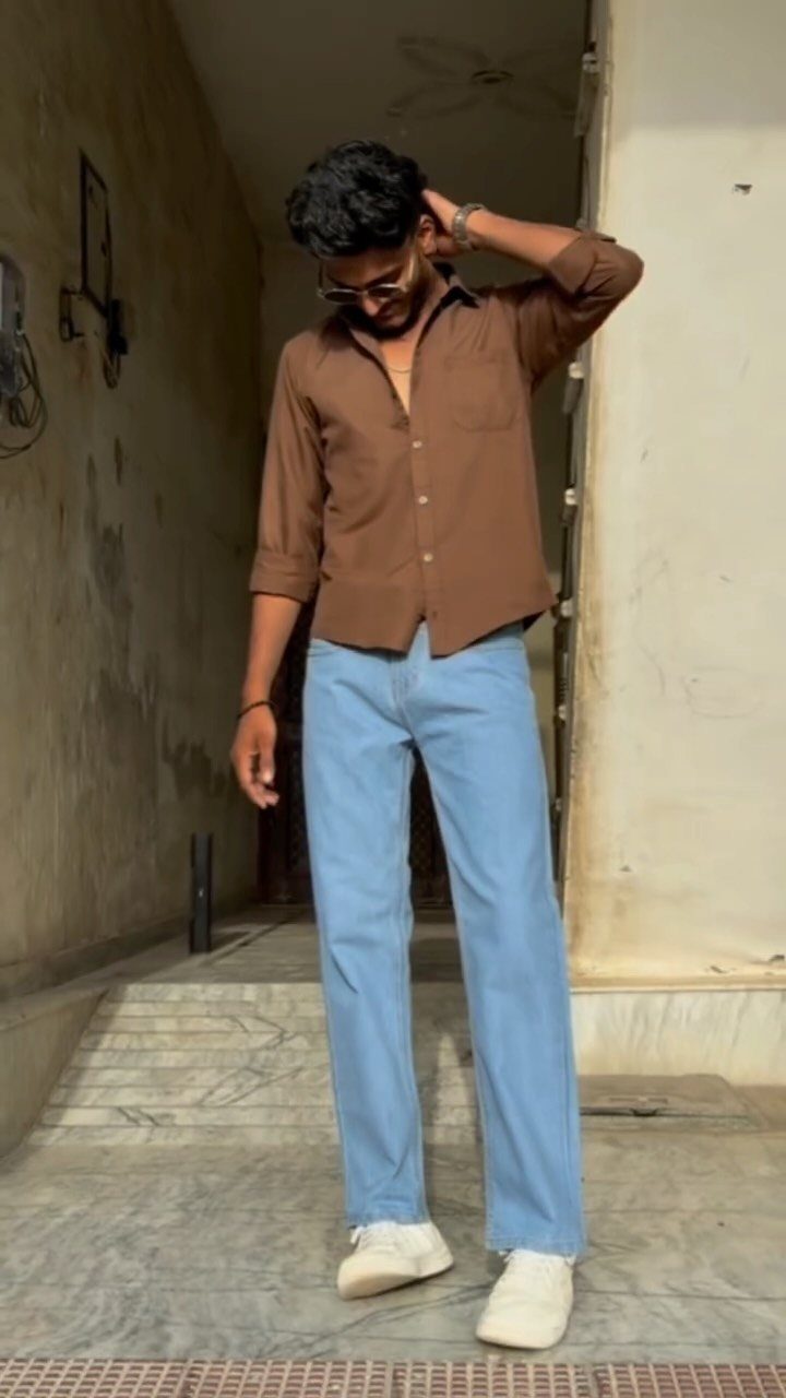 Man posing in a brown shirt, light blue jeans, and white sneakers.