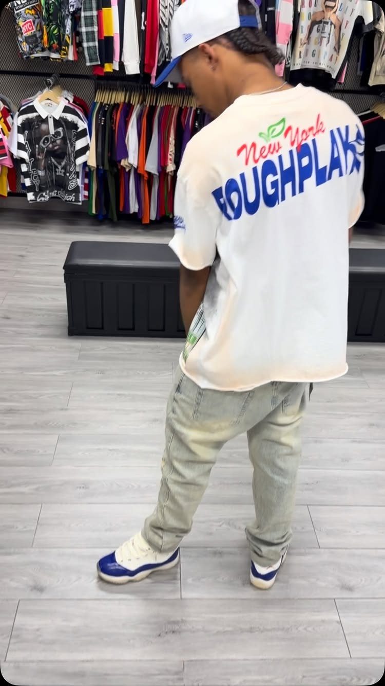 A person wearing a white graphic t-shirt, light blue jeans, and blue and white sneakers.