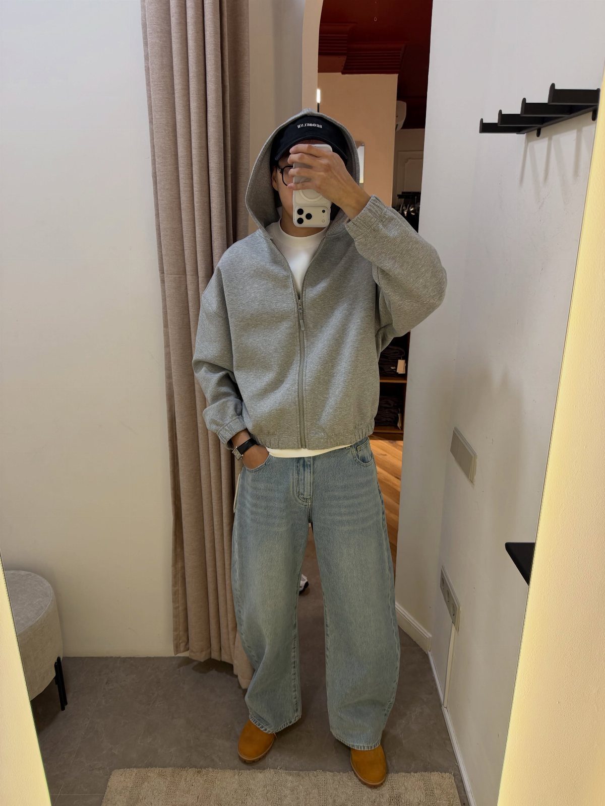 Person in a grey hoodie and light blue jeans posing for a mirror selfie.