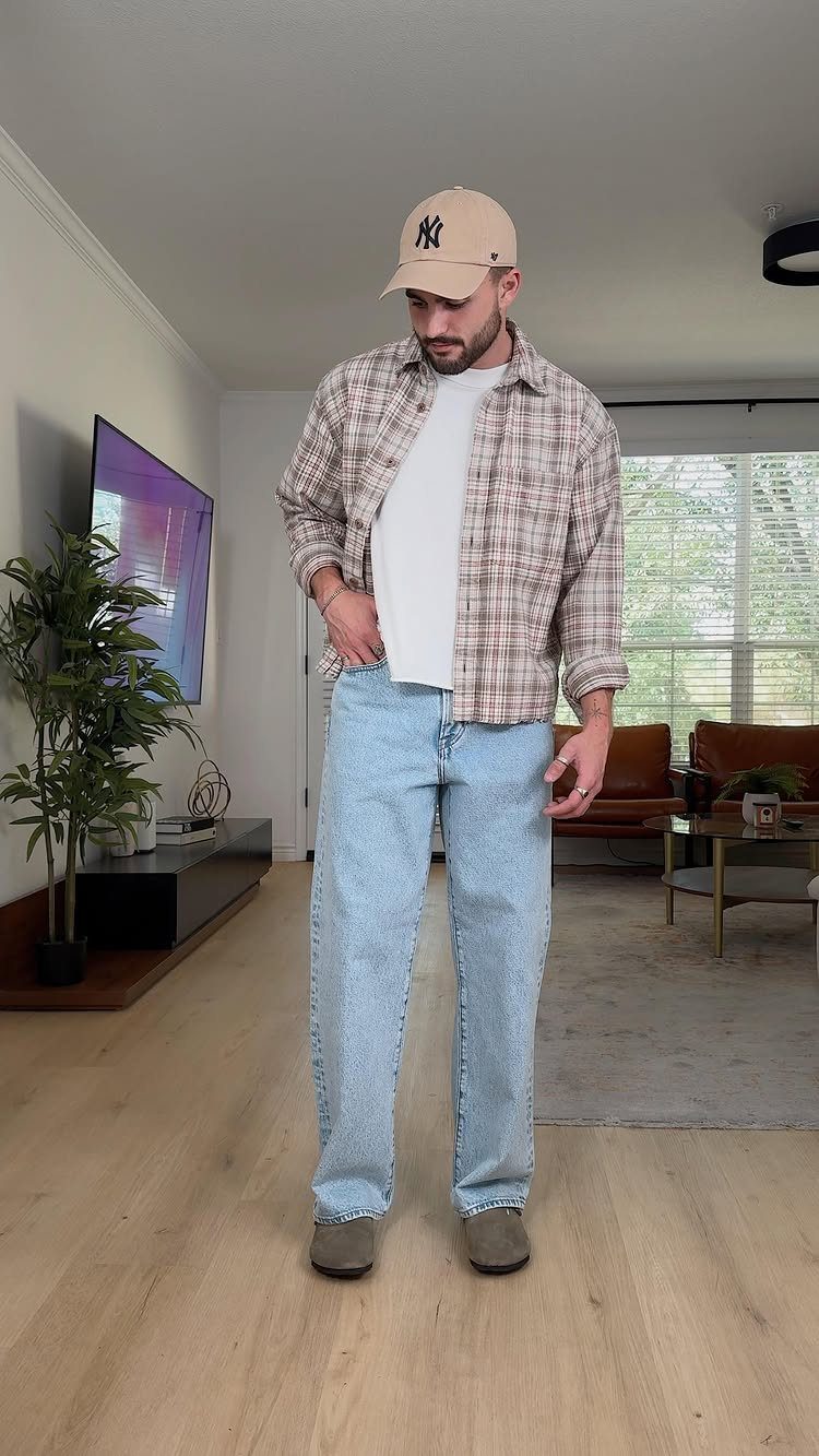 A man wearing a plaid flannel shirt over a white tee and light blue jeans.