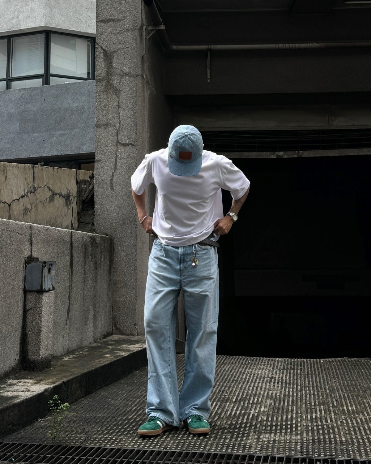 Person wearing a white t-shirt, light blue jeans, and green sneakers standing outdoors.
