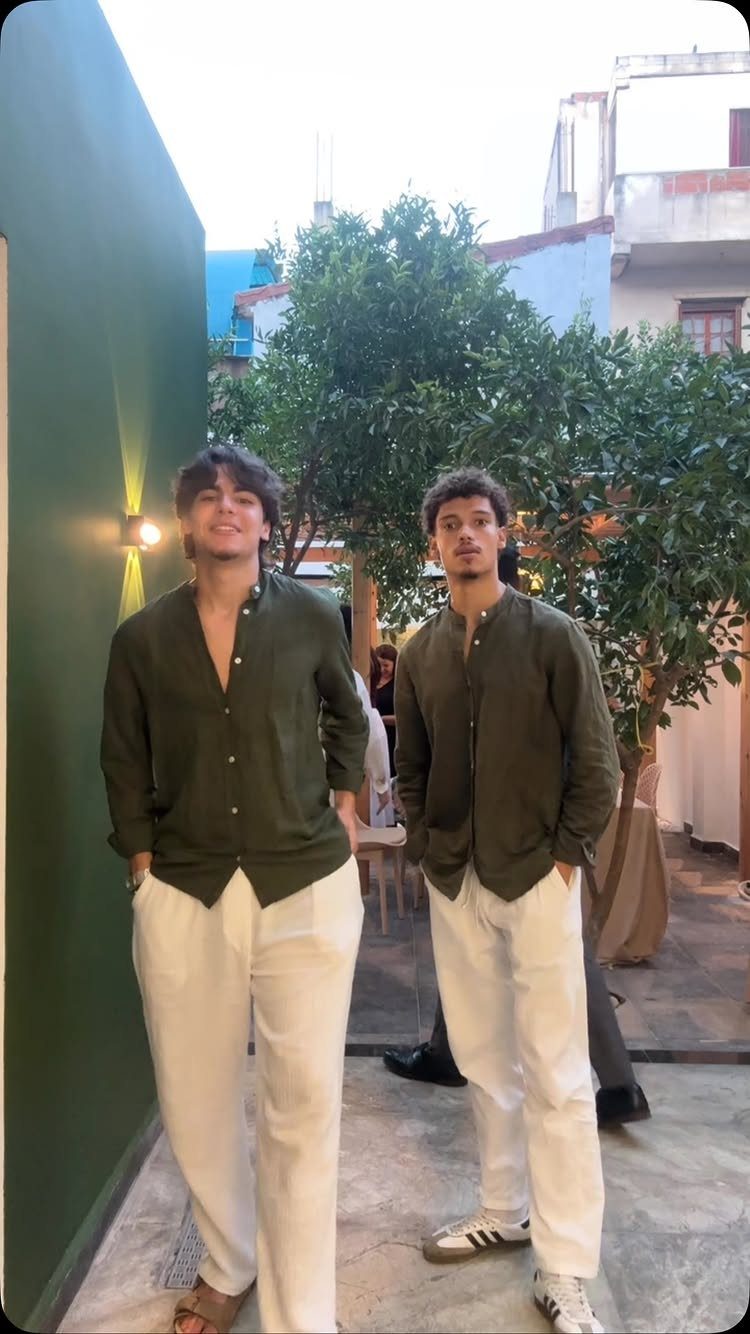 Two men wearing olive green linen shirts and white linen pants standing outdoors.