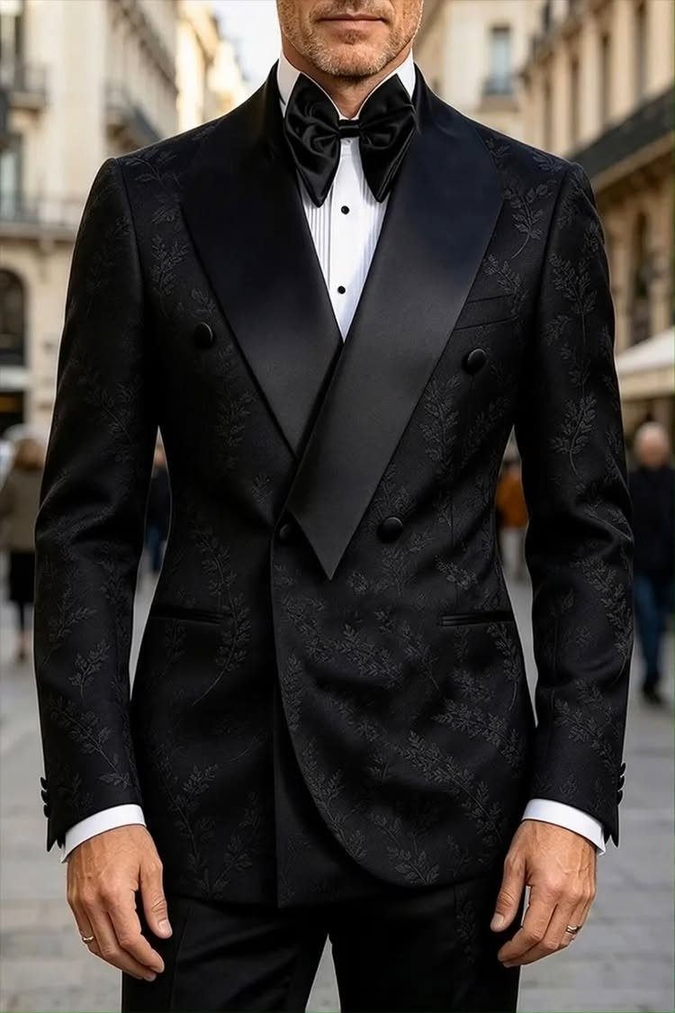 A man dressed in a formal black patterned tuxedo and bow tie.