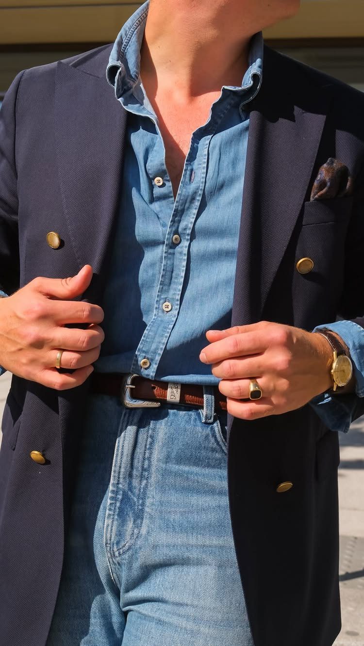 Man wearing a navy blazer, denim shirt, and denim trousers with a brown leather belt.