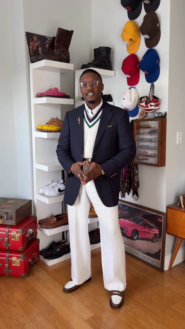 Man posing in a navy blazer, white sweater vest, and wide-leg white trousers.