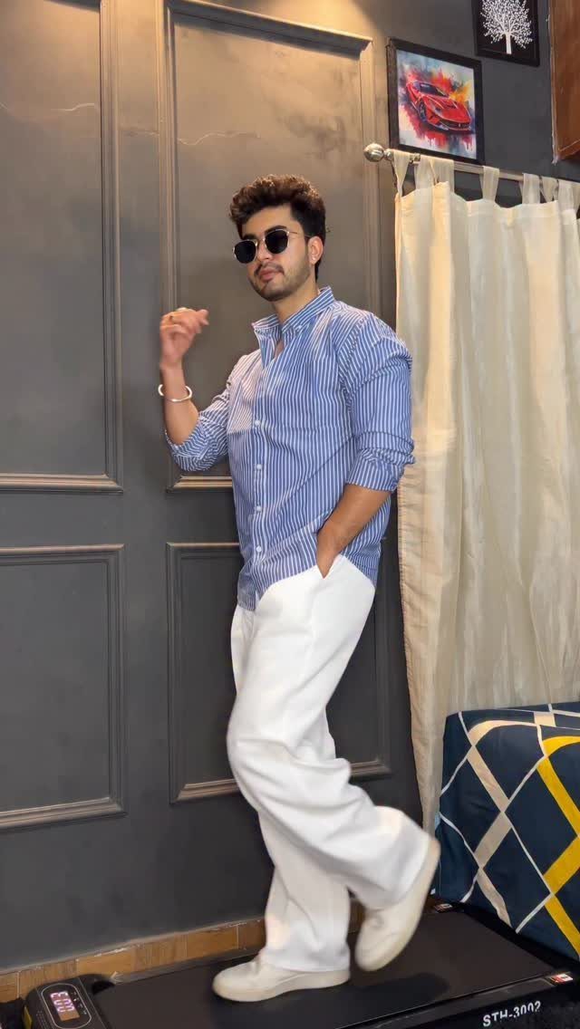 Man in a striped blue shirt and loose white pants posing indoors.