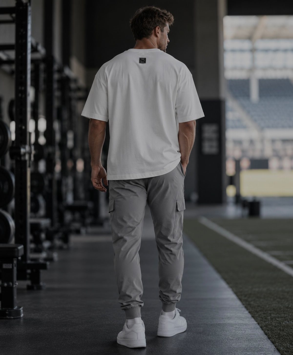 Man in white t-shirt and grey cargo joggers standing in a gym setting.