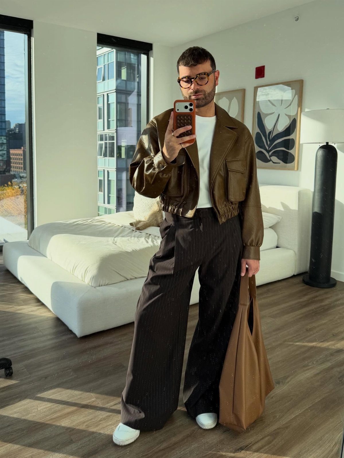 Man in a leather jacket and wide-leg trousers posing for a mirror selfie.