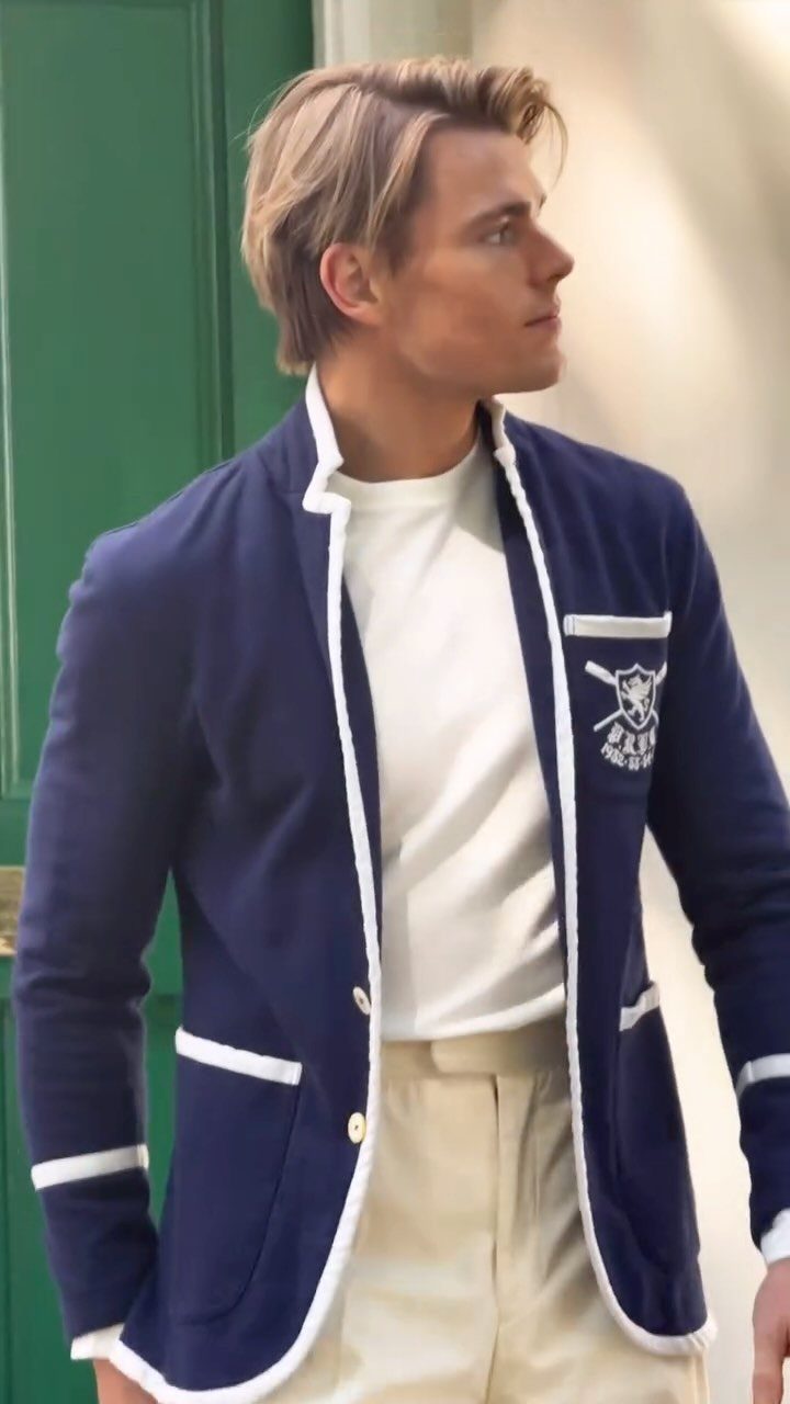 Blonde man wearing a navy blue cardigan with white trim and cream trousers.