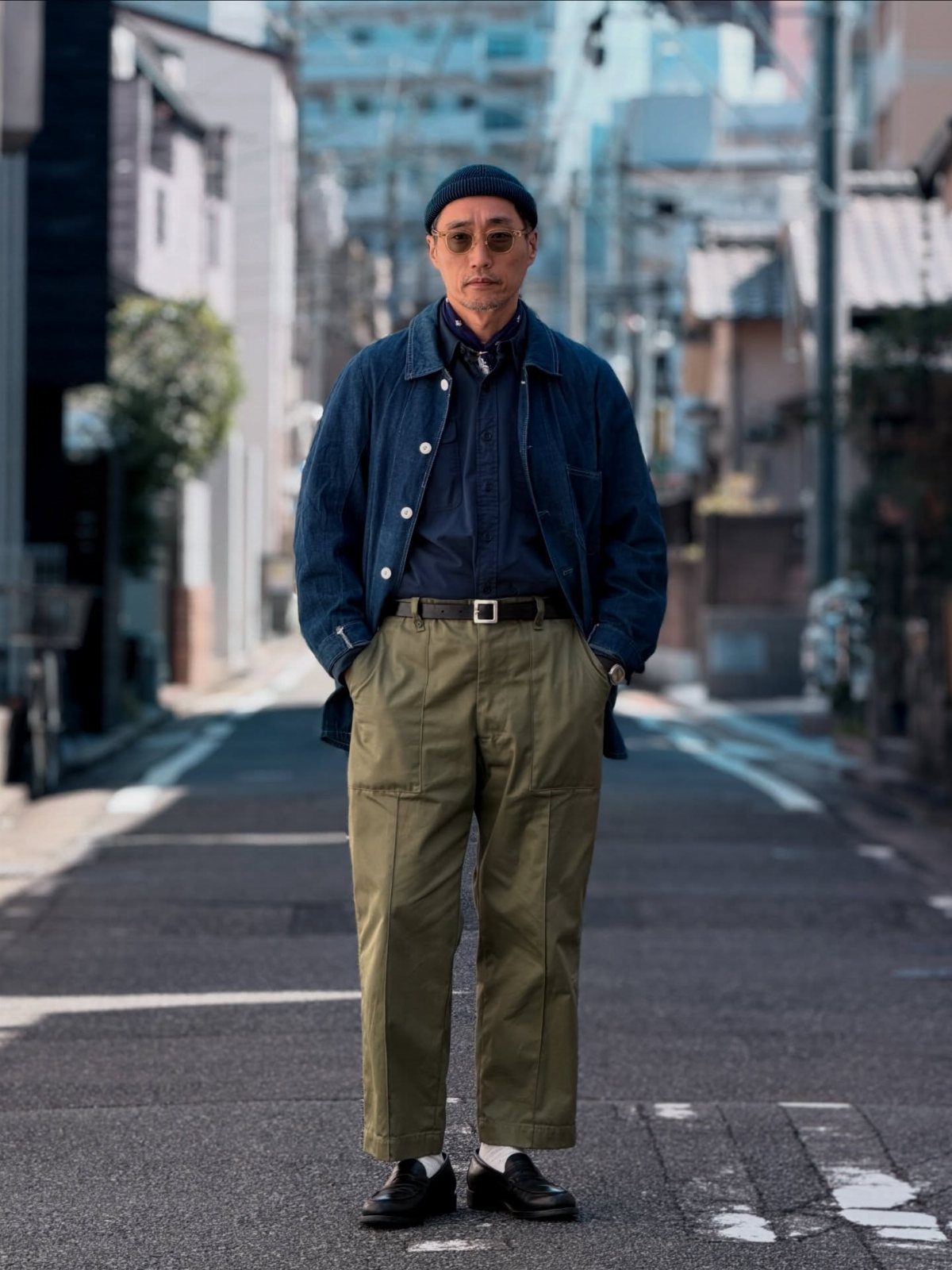 Man in navy jacket and olive utility trousers standing on a city street.