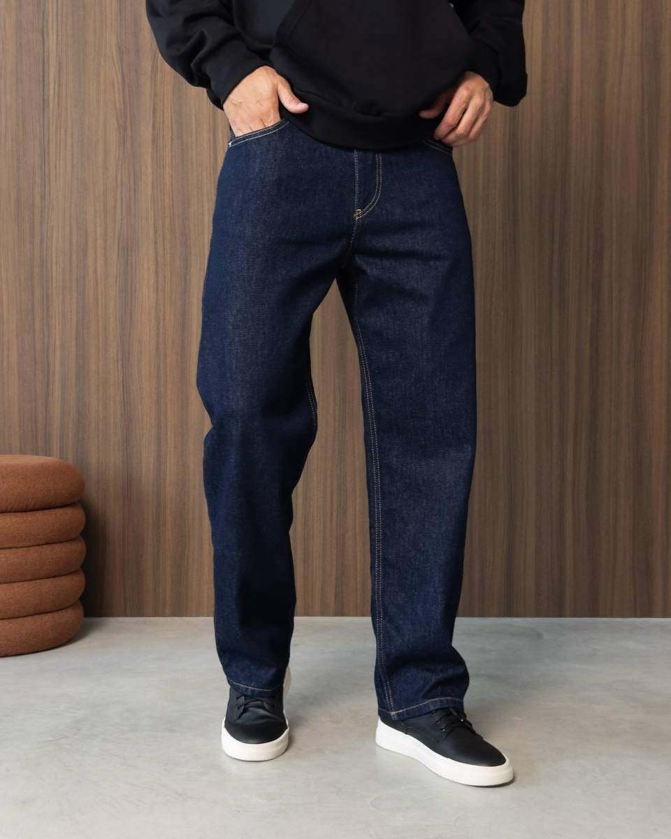 A person wearing dark wash denim jeans and a black sweatshirt with black sneakers.
