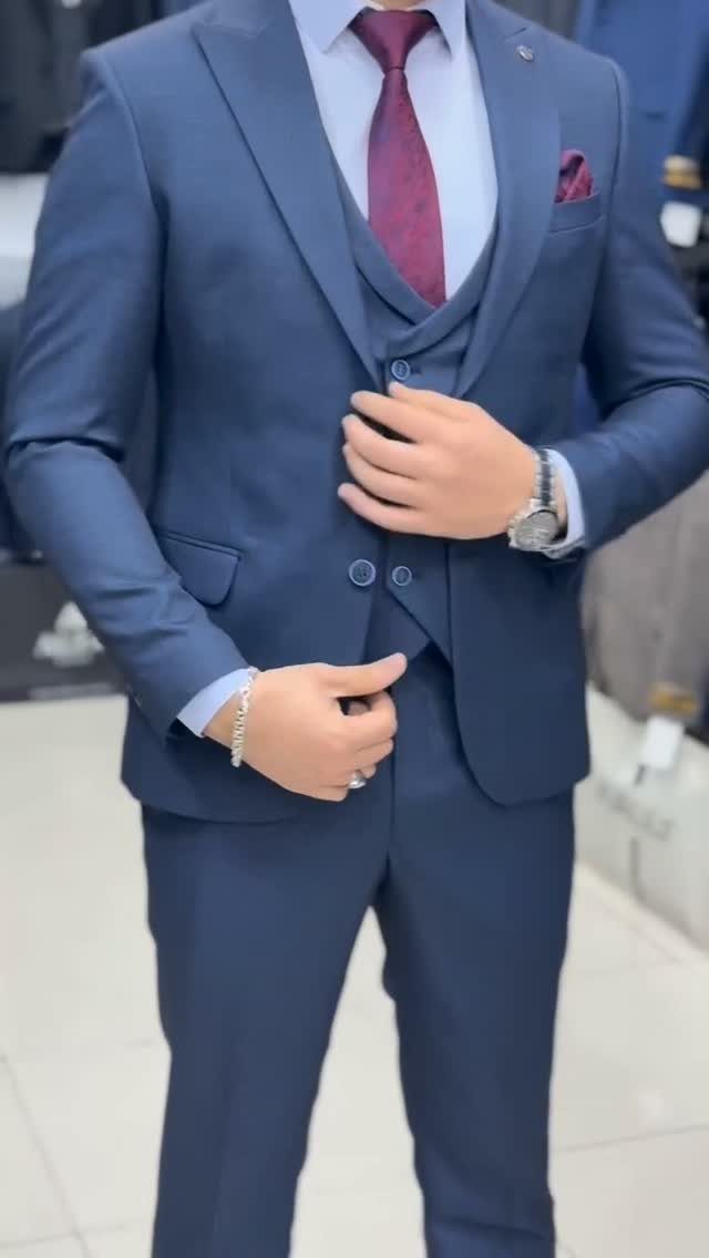 Man wearing a tailored navy blue three-piece suit with a maroon tie and pocket square.