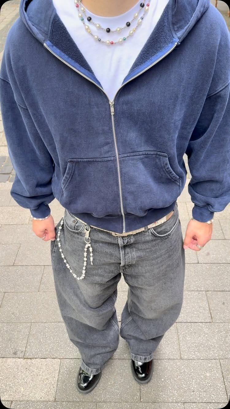 A person wearing an oversized navy hoodie, white t-shirt, and baggy grey jeans with a silver chain belt.