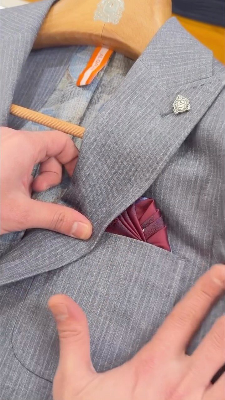Hands adjusting a grey textured blazer featuring a burgundy silk pocket square.