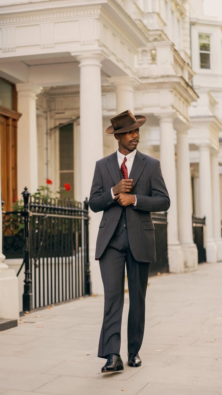 Man in a dark pinstripe suit and brown fedora walking past white columns.