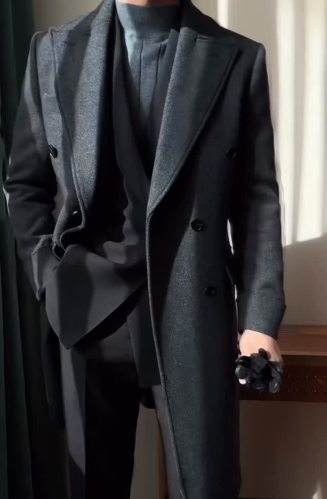 Man wearing a dark charcoal grey overcoat, suit, and grey turtleneck sweater.