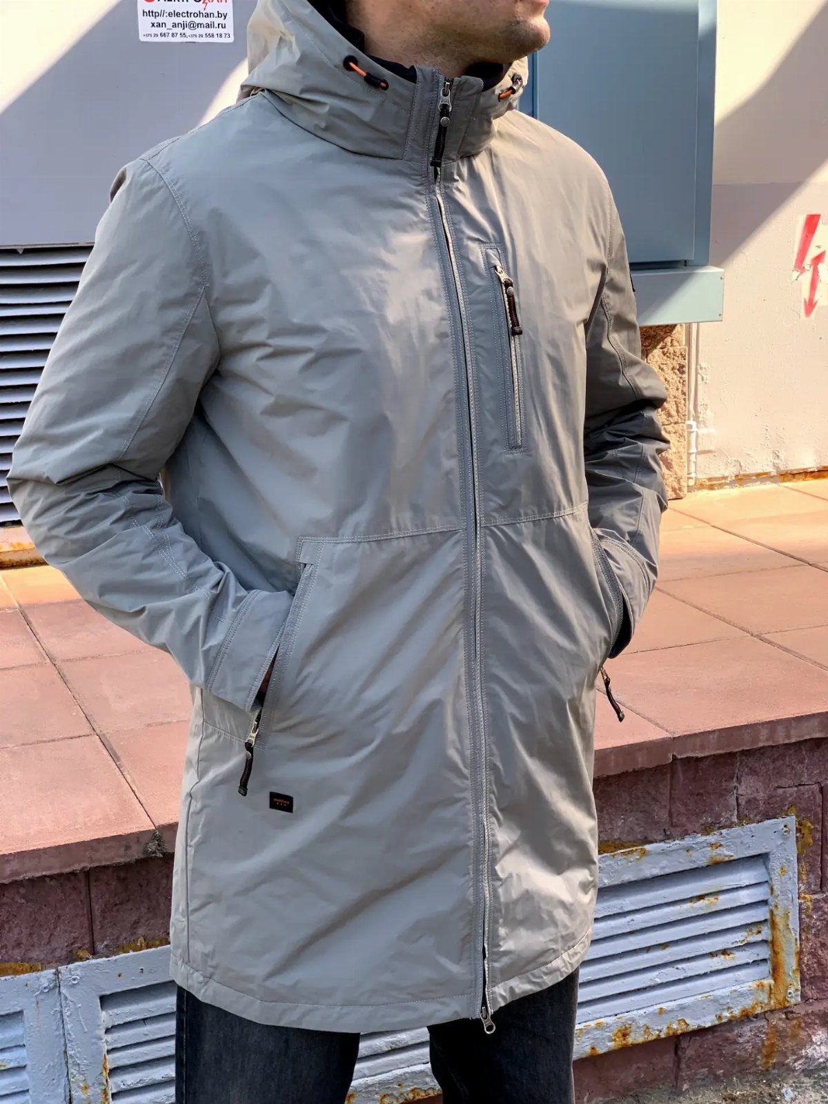 Man wearing a light grey lightweight parka and dark denim jeans standing outdoors.