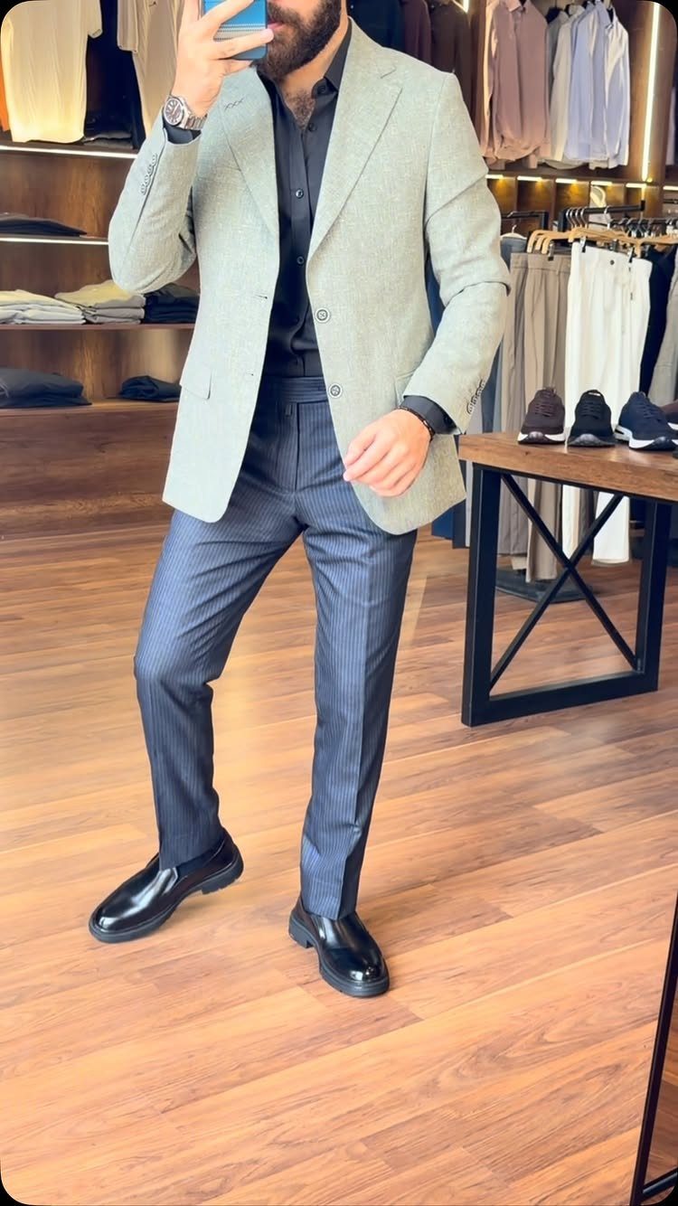 Man wearing a light grey blazer, dark shirt, and pinstripe trousers standing in a boutique.