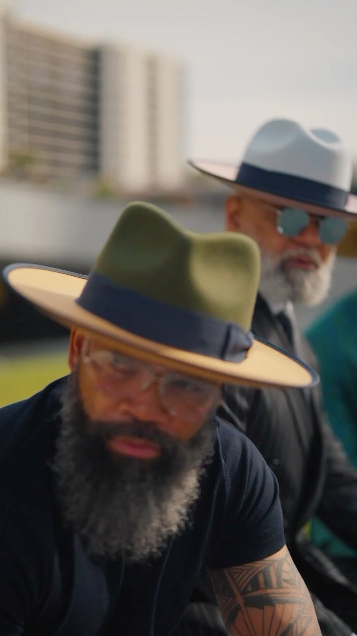 Two bearded men wearing stylish wide-brimmed fedora hats outdoors in a city setting.