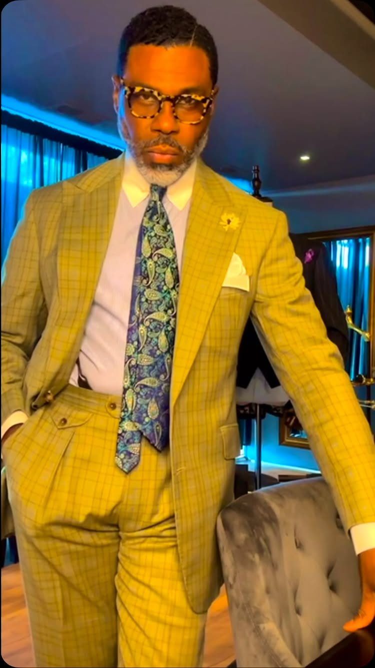 Man in a yellow plaid suit, white shirt, and blue patterned tie standing indoors.
