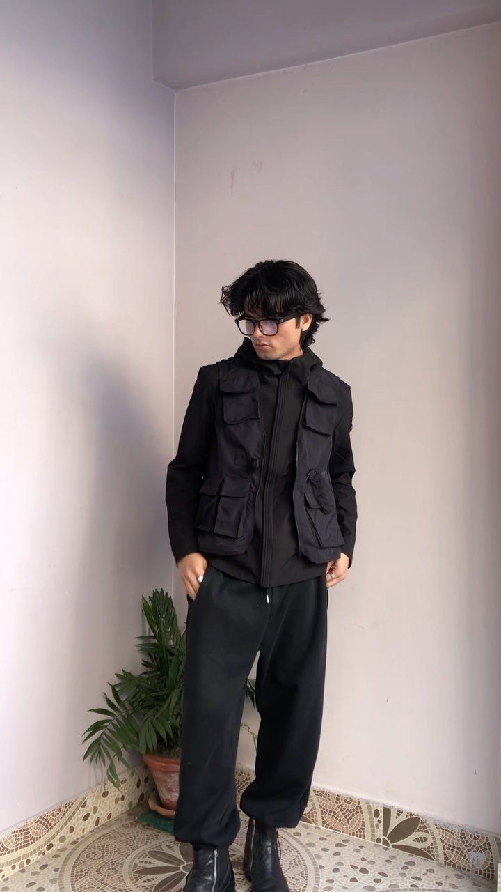Man wearing a black tactical utility vest with large pockets over a black hoodie and pants.