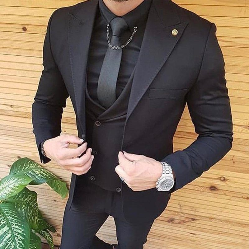 Man wearing an all-black formal suit with a waistcoat and tie.