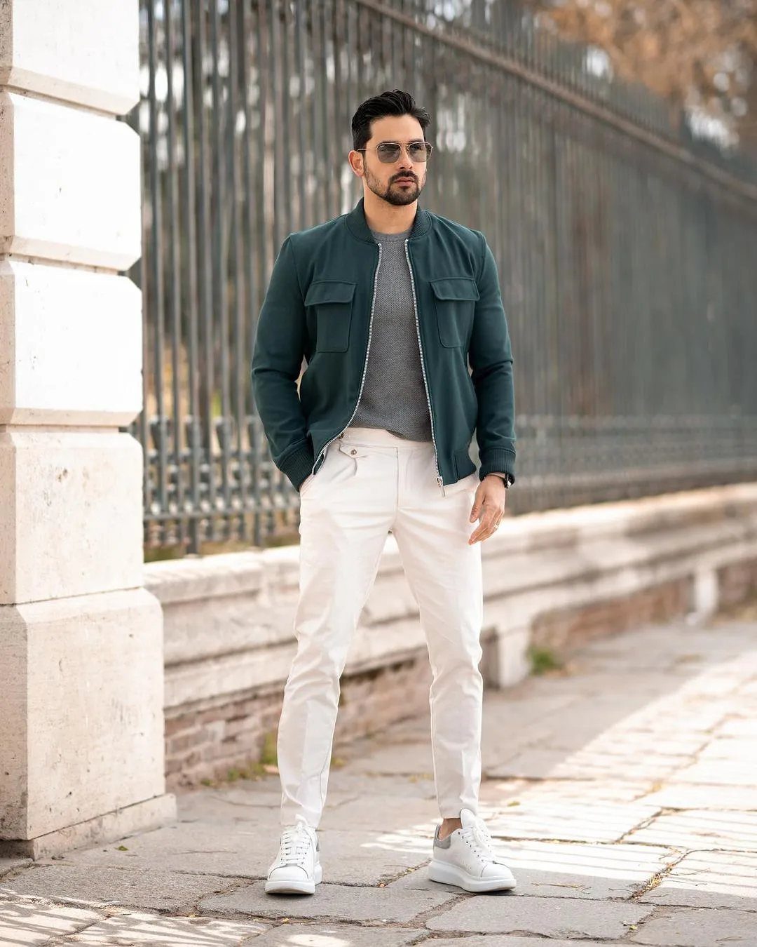 Man with groomed beard and styled hair wearing a green jacket and white trousers.