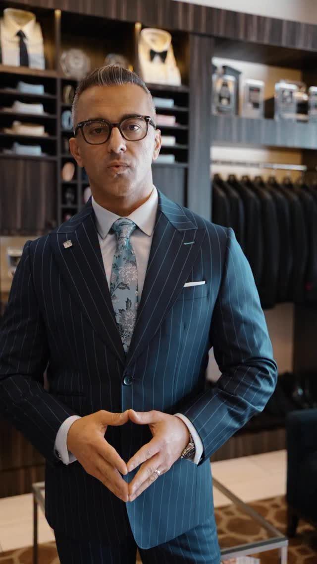 Man in a navy pinstripe suit and patterned tie standing in a luxury clothing store.