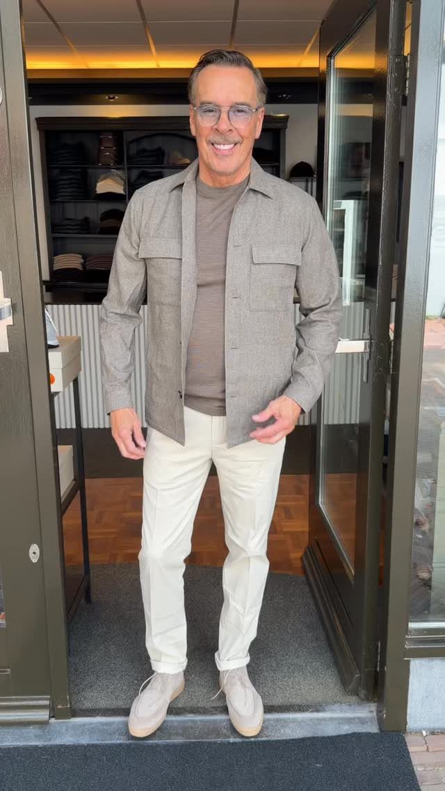 Middle-aged man smiling while wearing a grey shirt, brown t-shirt, white trousers, and beige shoes.