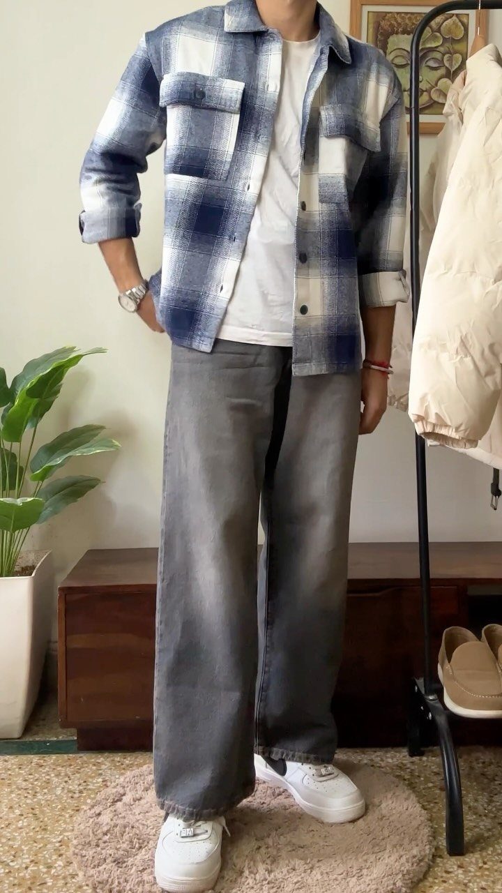 Man wearing a blue plaid flannel shirt, white t-shirt, and grey jeans with white sneakers.