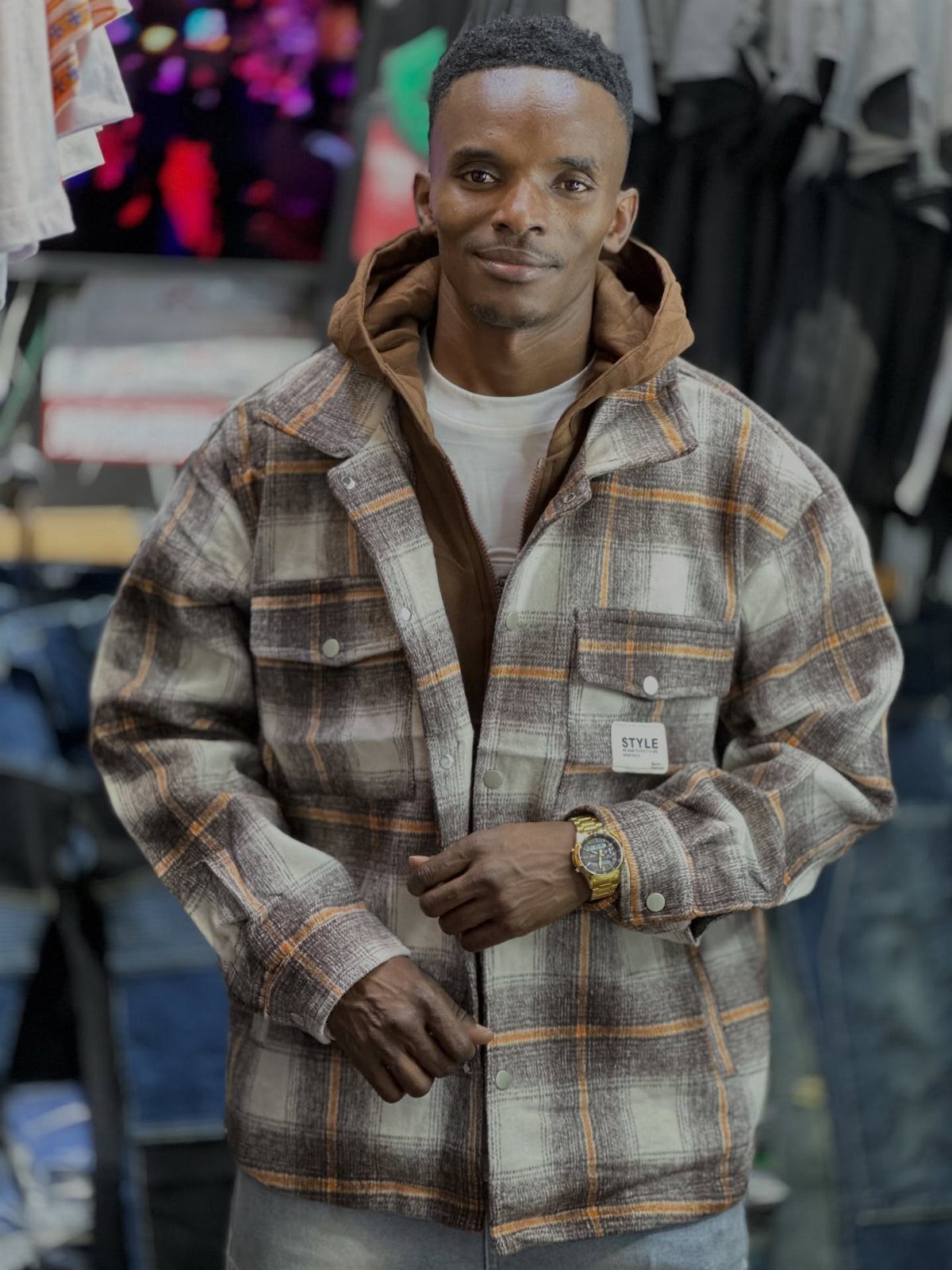 Man wearing a brown hoodie underneath a plaid flannel shirt in a clothing store.