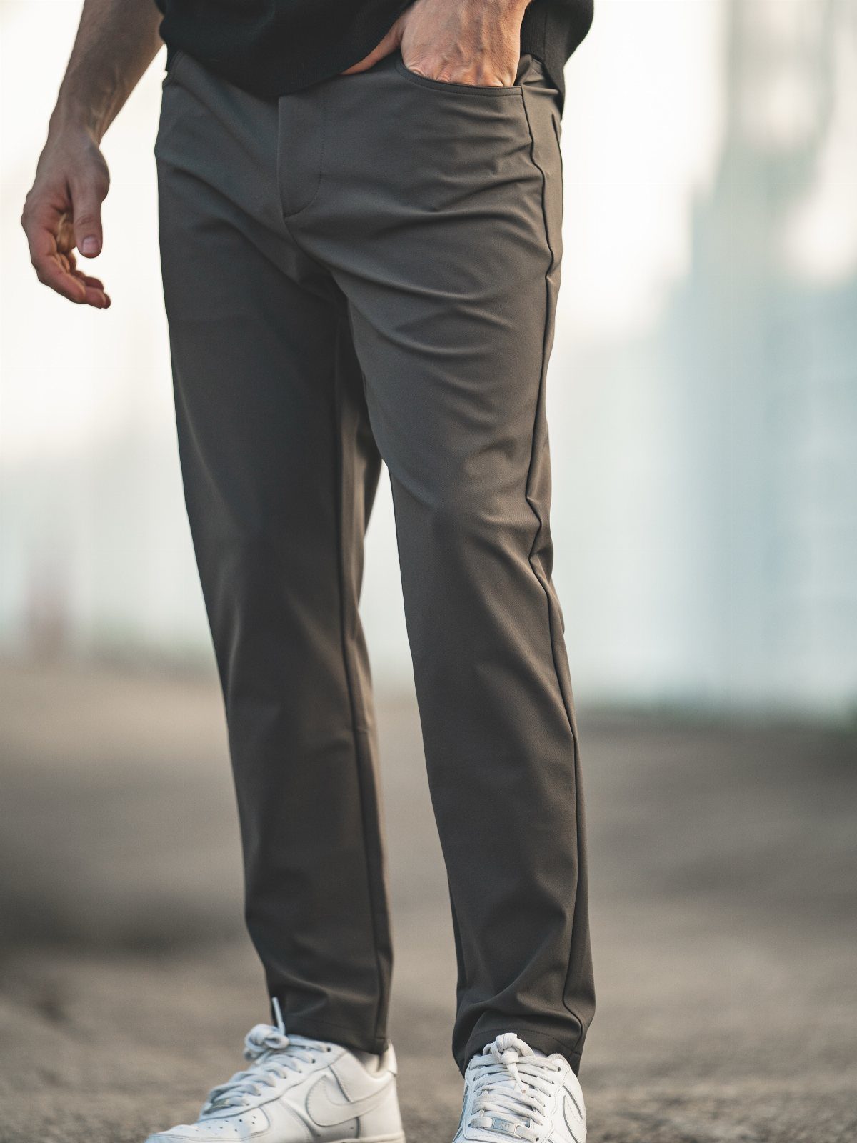 Man wearing dark grey slim-fit casual trousers and white sneakers standing outdoors.