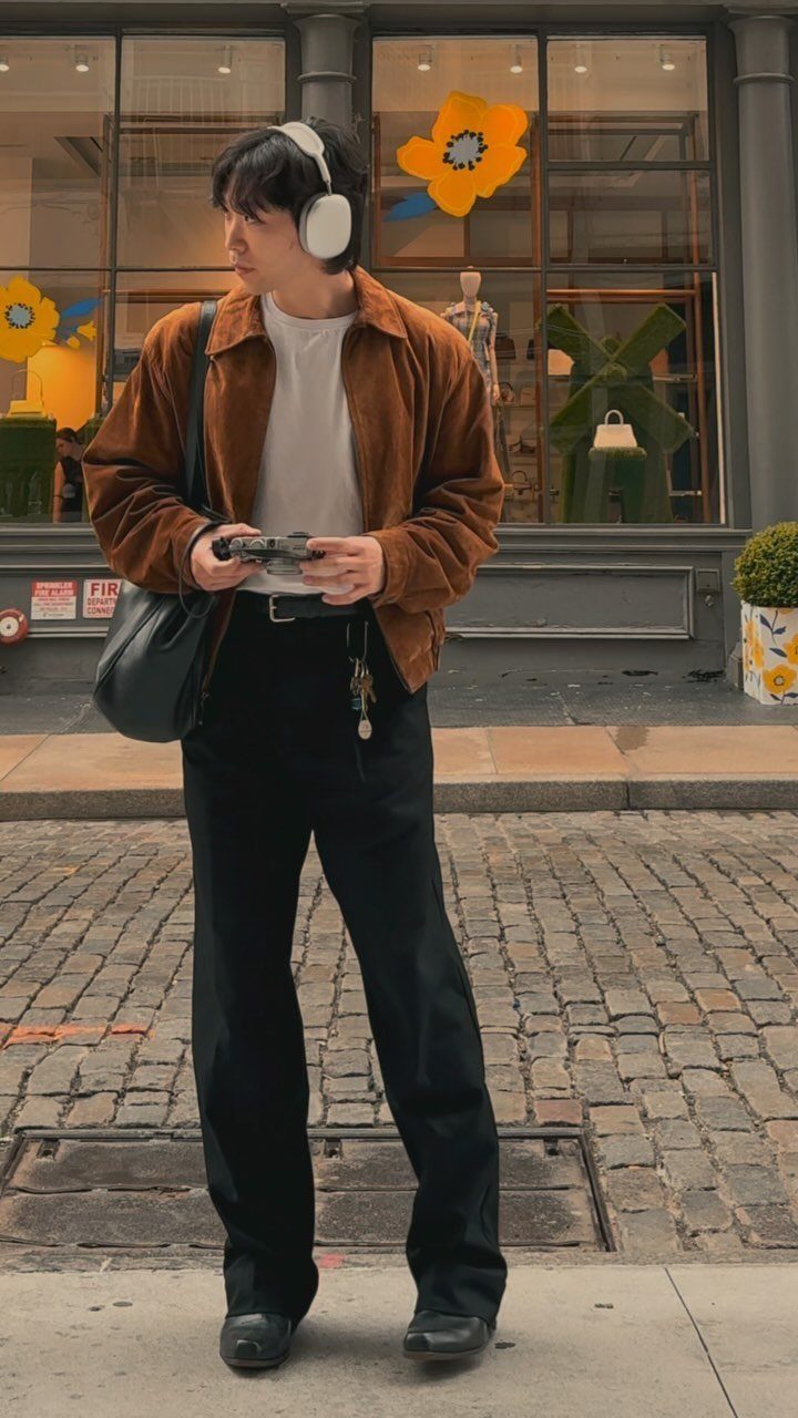 Man in a brown suede jacket and black trousers standing on a cobblestone street.