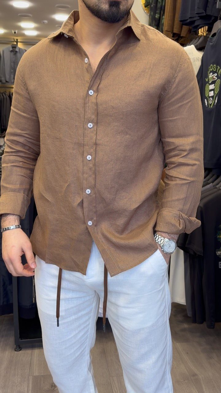 Man wearing a brown linen button-down shirt and white drawstring trousers in a clothing store.