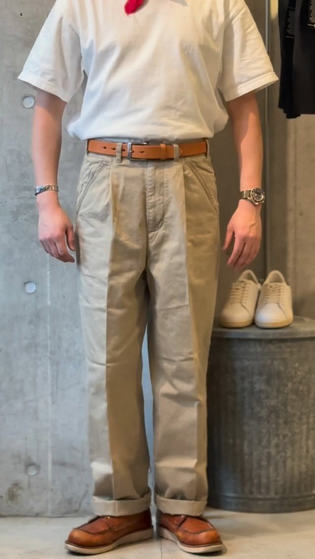 A person wearing tan chino pants, a white t-shirt, and brown leather shoes.