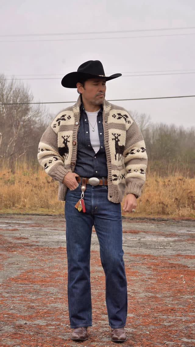 Man in a black cowboy hat and a patterned Cowichan knit sweater standing outdoors.