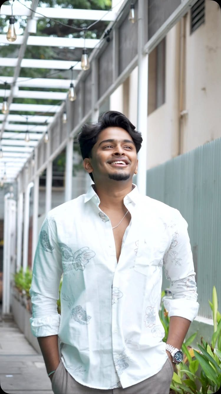 Smiling man wearing a white button-down shirt with subtle floral and butterfly patterns.