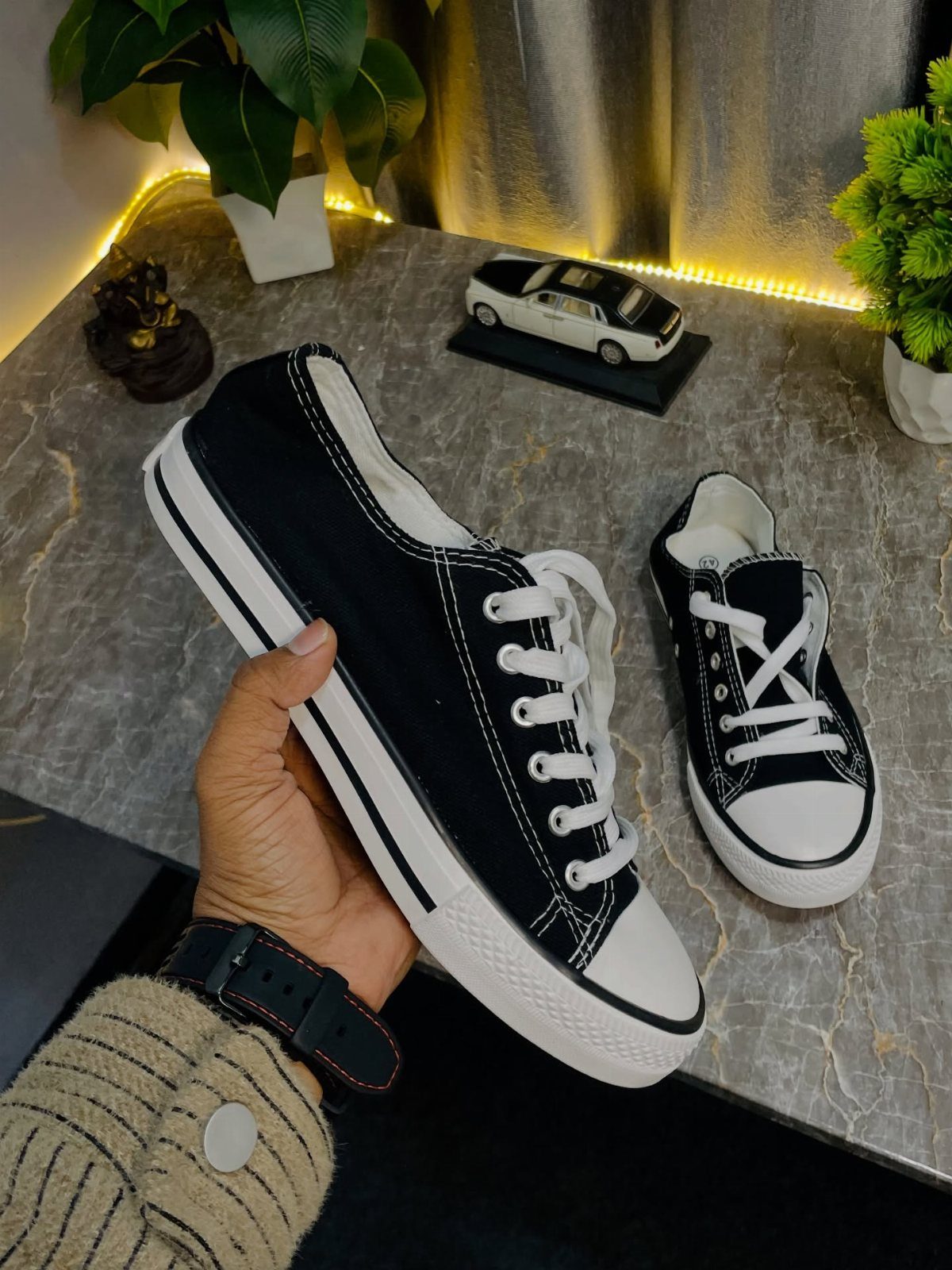 A hand holds a black canvas sneaker with white laces over a marble surface.