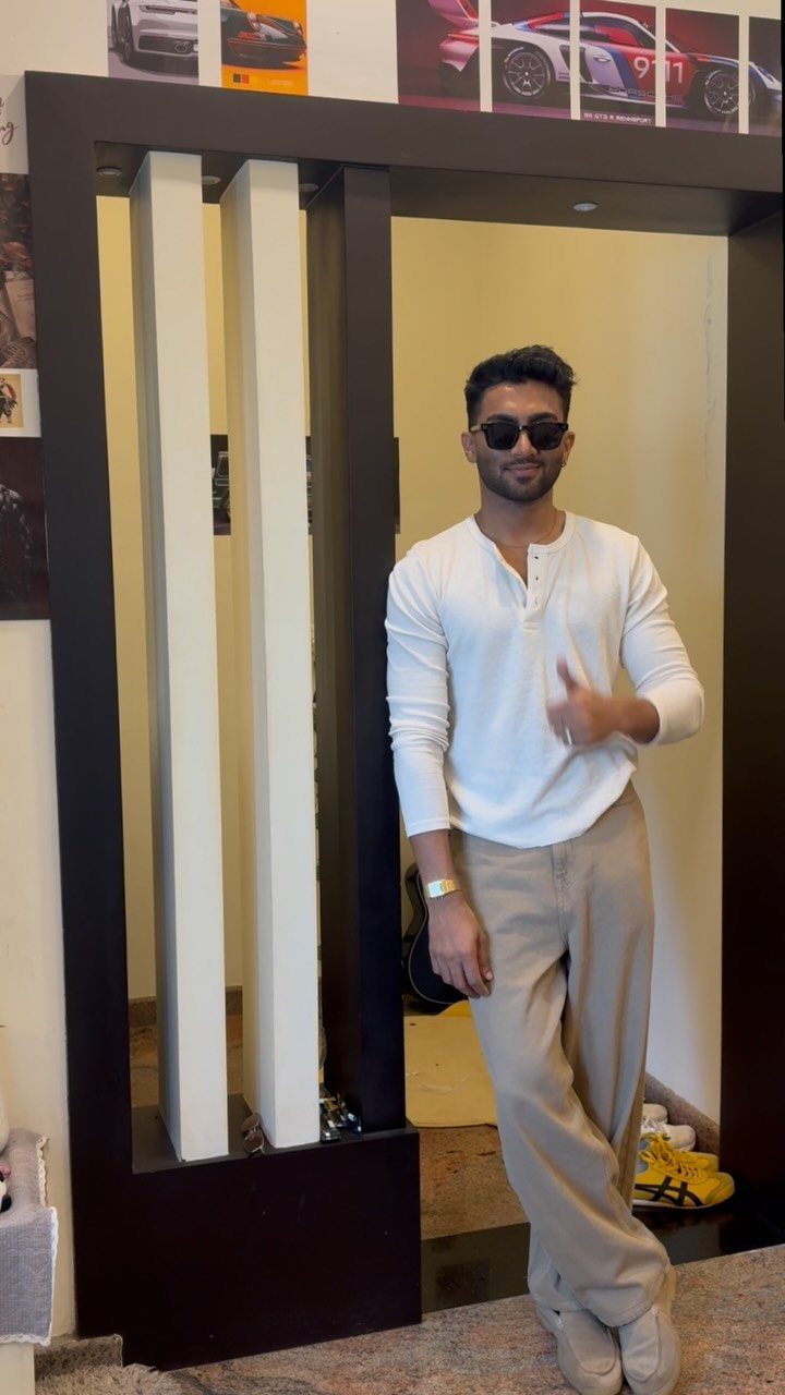 A man in a white long-sleeved Henley shirt and beige trousers posing indoors.