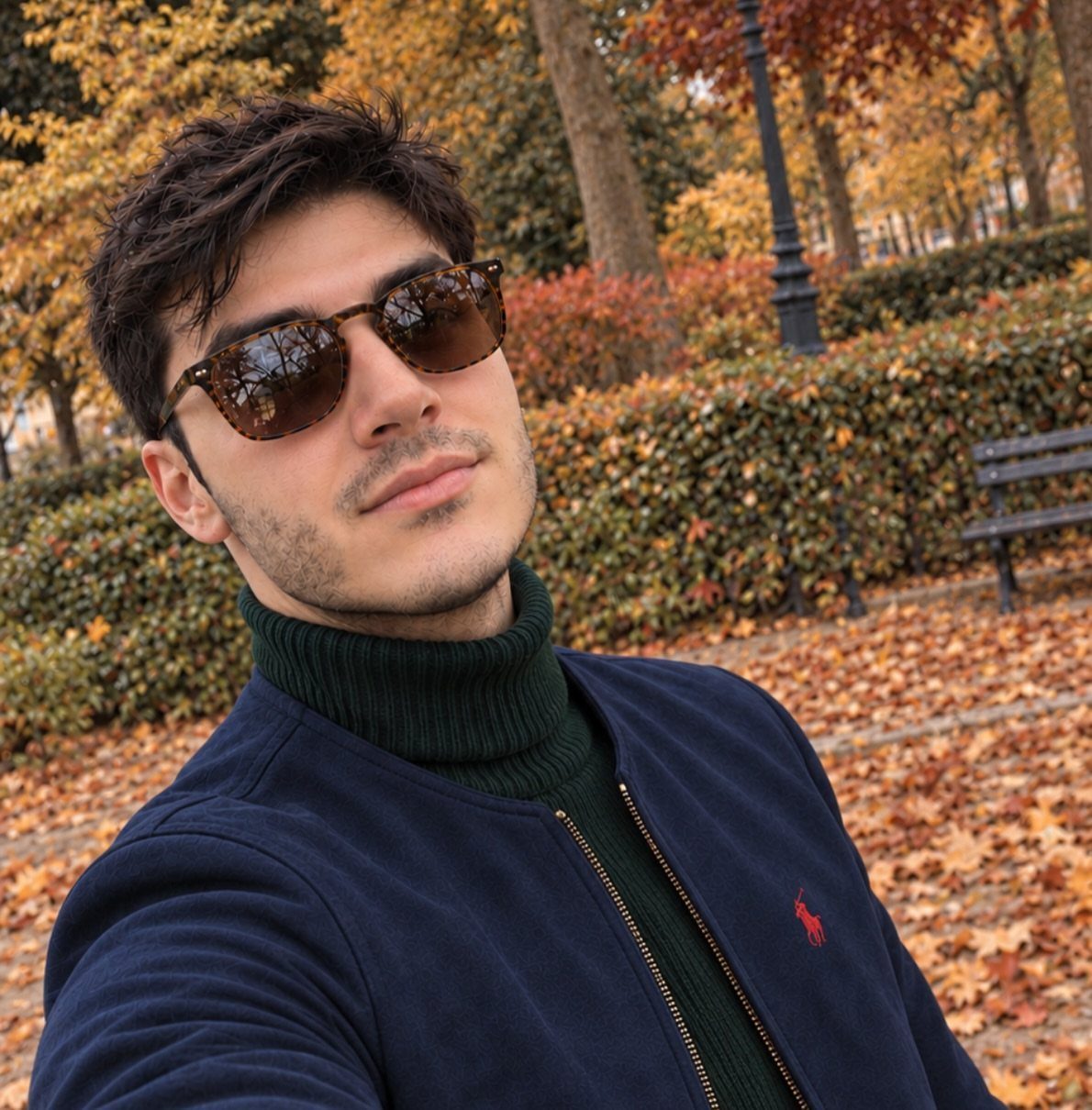 Man wearing a dark green turtleneck and navy bomber jacket in an autumn park.