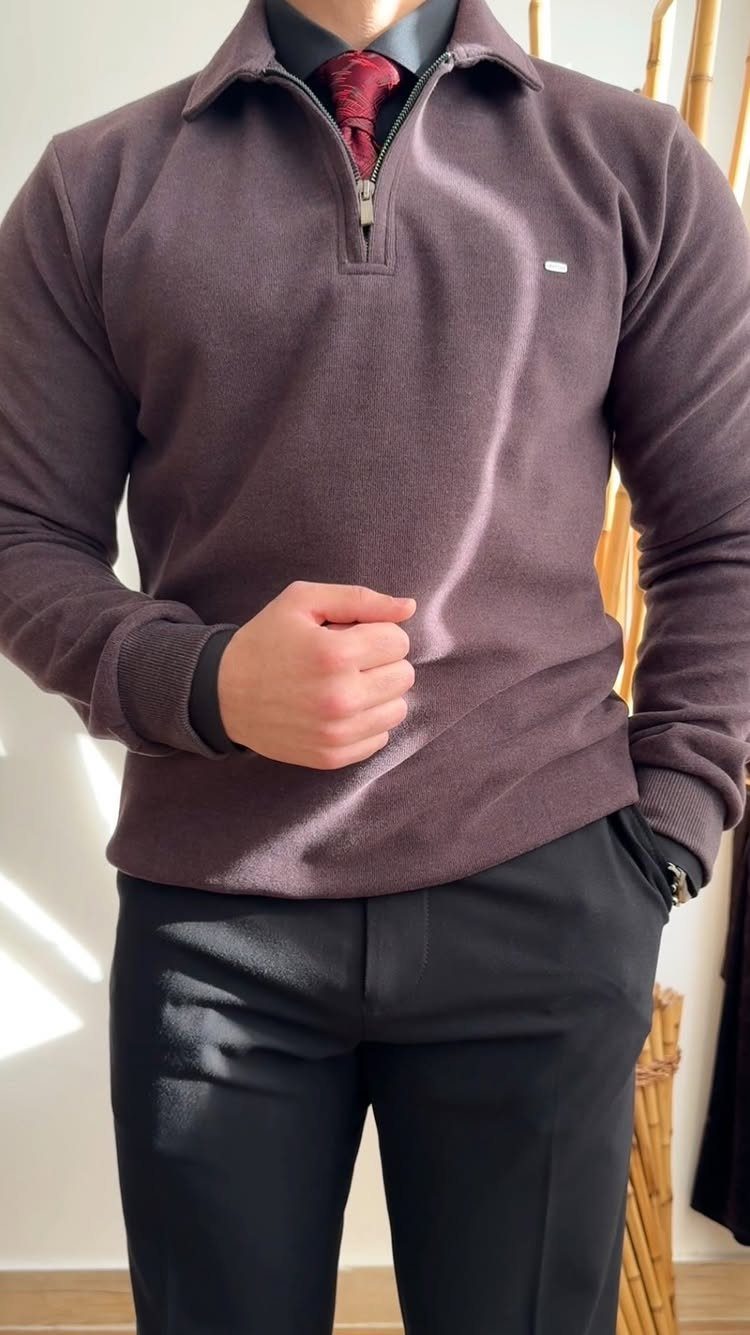 Man wearing a mauve quarter-zip sweater, red tie, and black trousers.