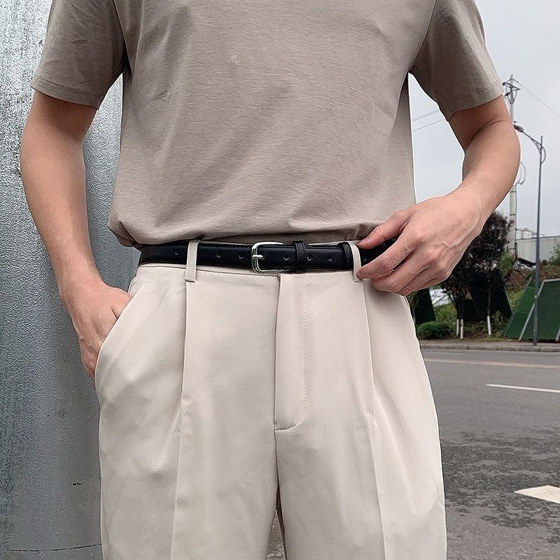 Man wearing cream pleated chinos with a black leather belt and a beige t-shirt.